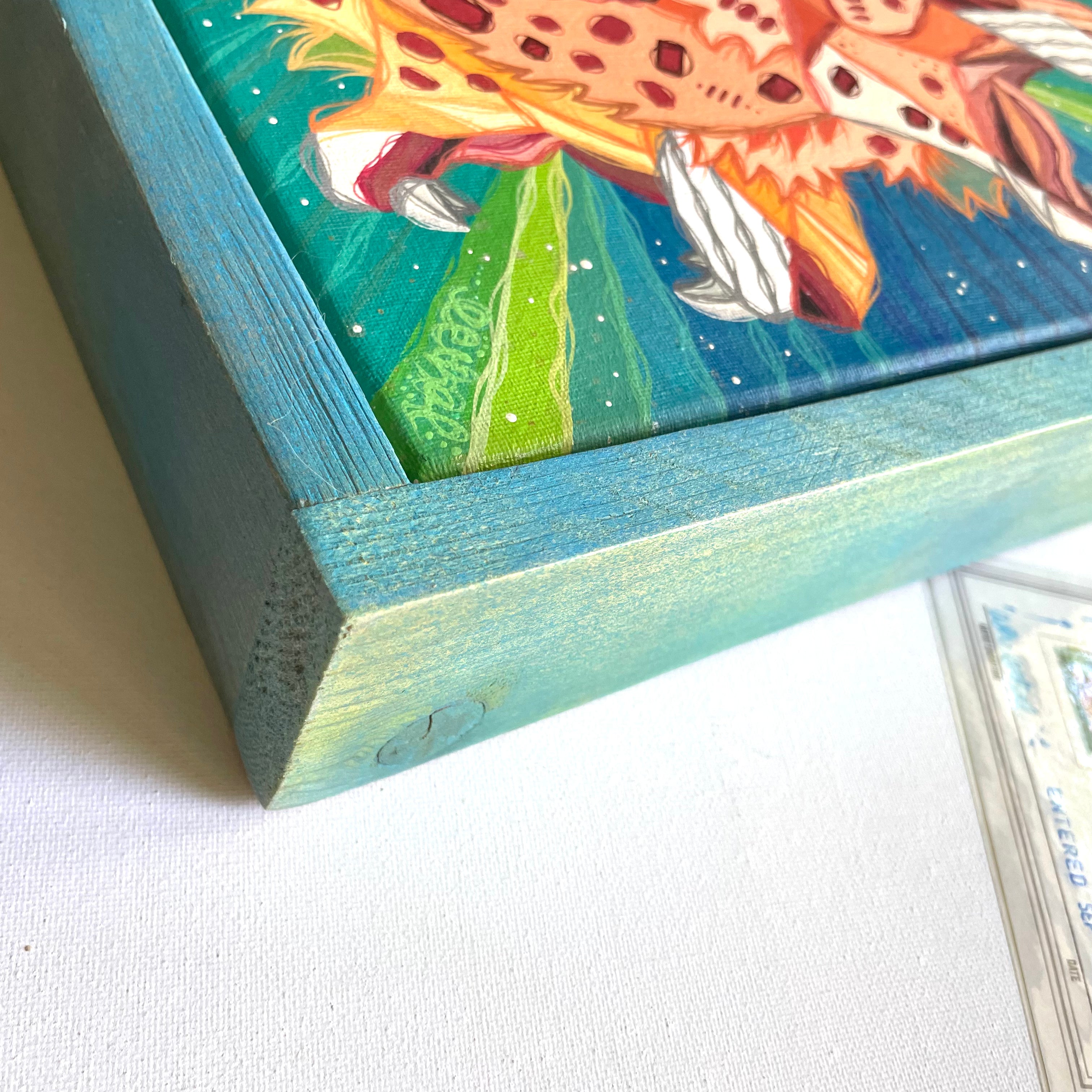 Close-up of a framed painting with a colorful subject on a white surface