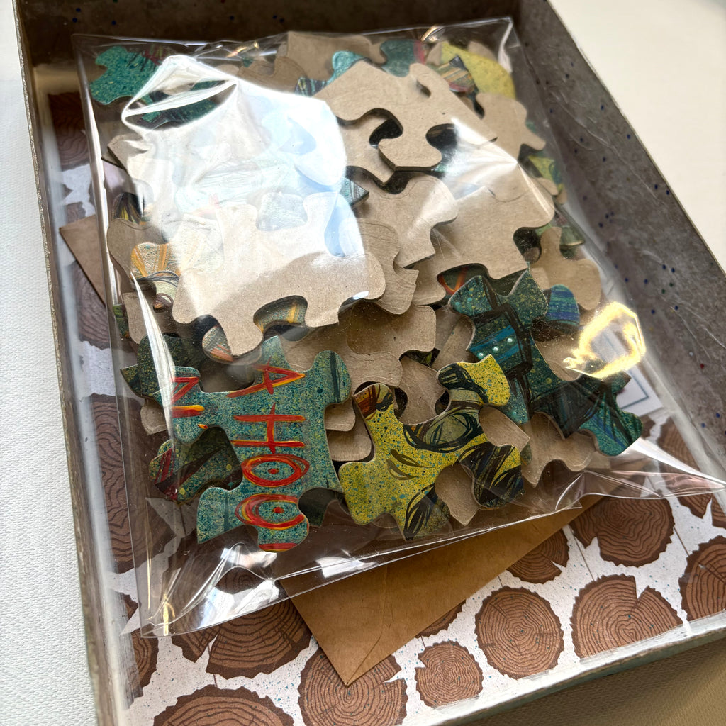 Jigsaw puzzle pieces in a clear plastic bag with a wooden box by Ash Lethal