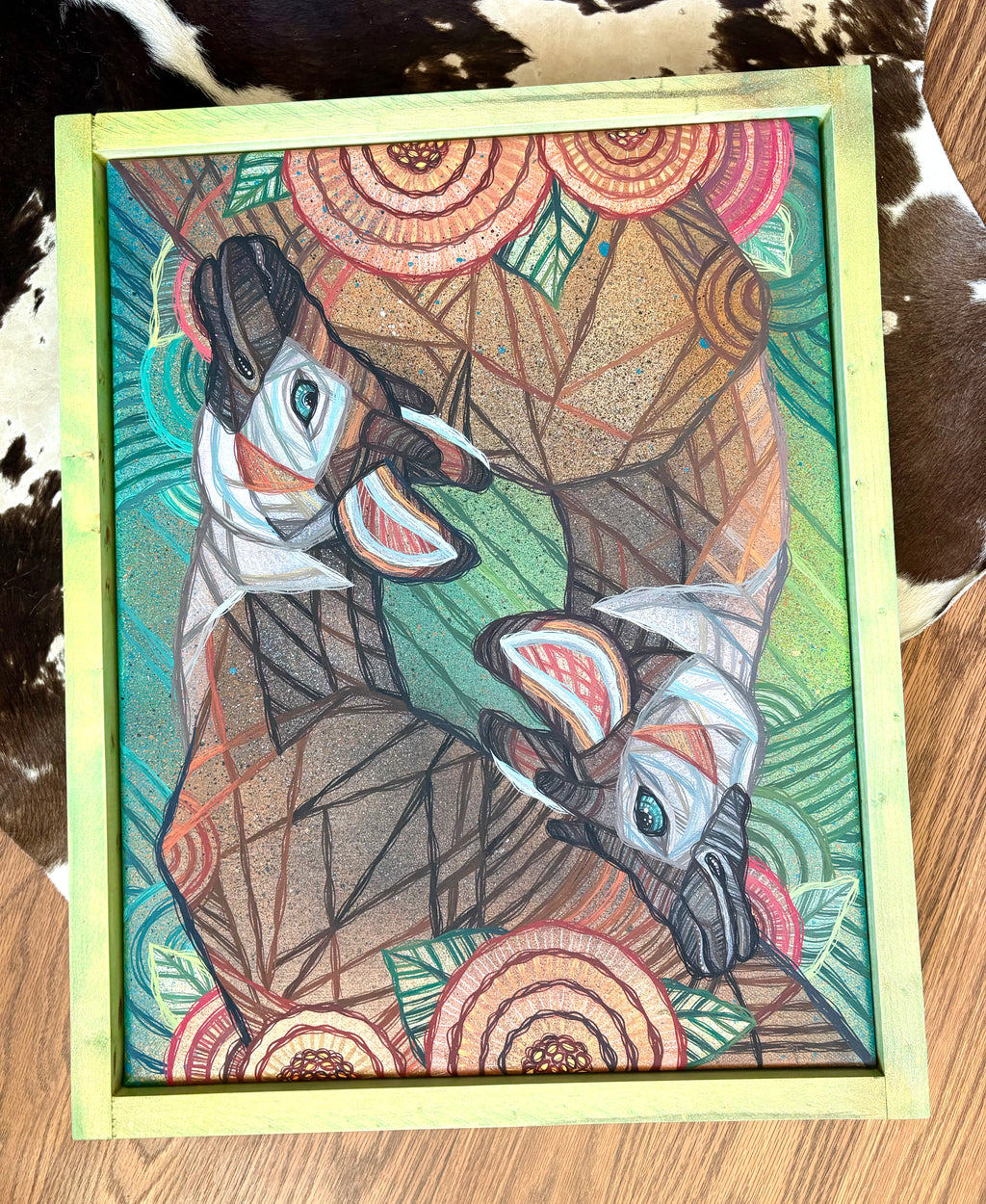Colorful artwork of two okapi animals on a wooden surface with a cowhide rug in the background