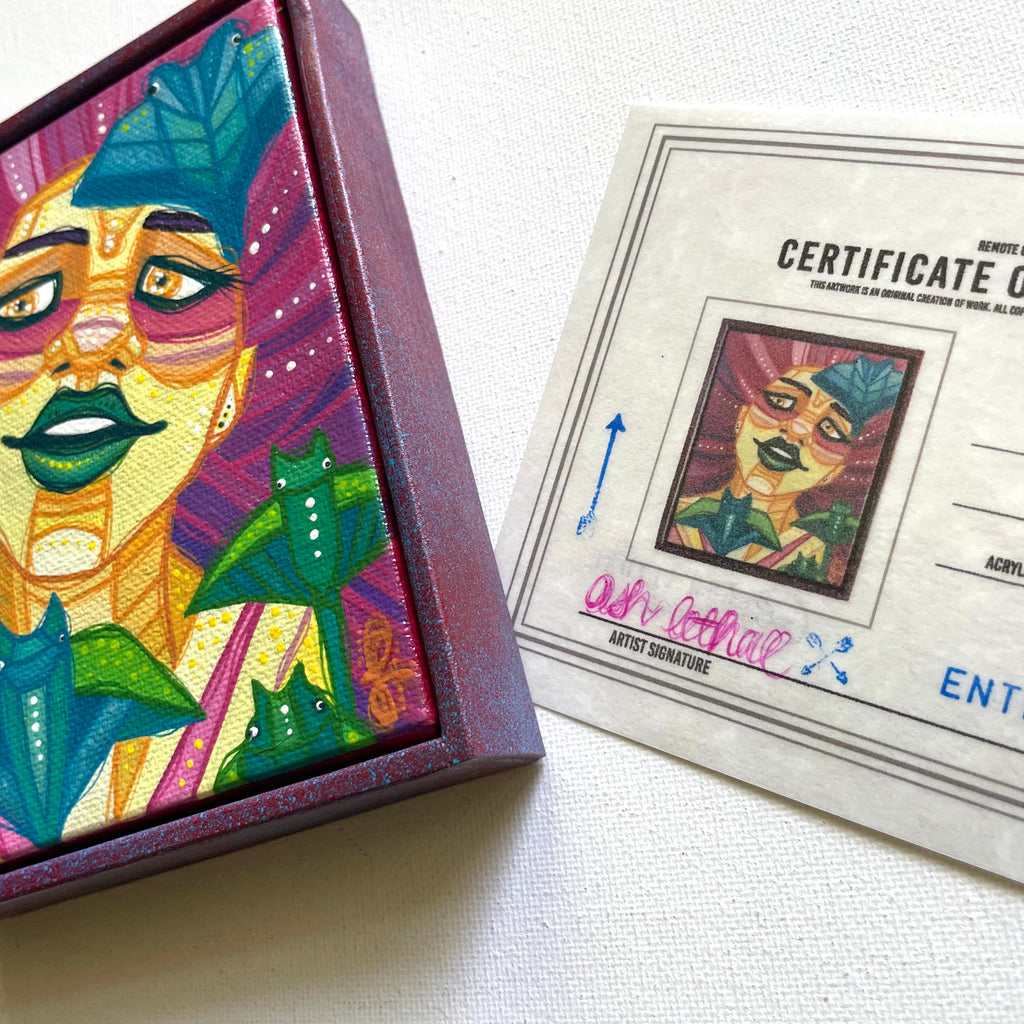 Colorful art piece with a face and manta rays, next to a certificate of authenticity on a white surface.